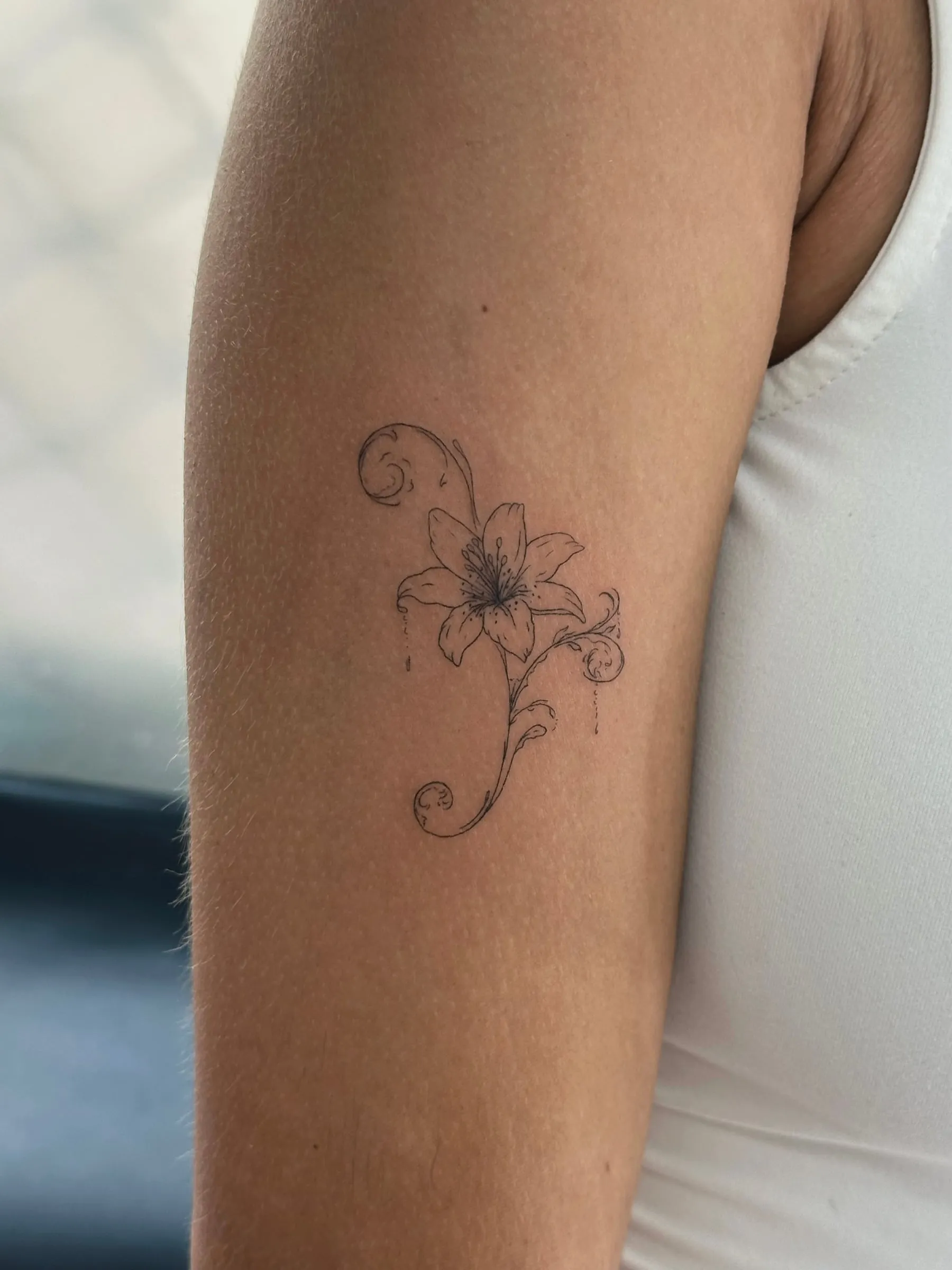 Azucena en línea fina con volutas ornamentales, en el brazo